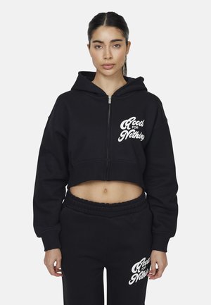 Felpa nera corta con chiusura a zip, caratterizzata da testo bianco "Good for Nothing" sul petto, realizzata in un materiale morbido. Abbinata a pantaloni neri.