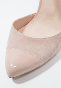 Chaussure plate pour femme beige avec bout pointu en cuir verni et tige en daim, présentée en gros plan sur fond blanc.