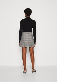 Schwarzes, geripptes Langarmoberteil kombiniert mit einem karierten Minirock. Der Rock hat eine ausgestellte Form in Schwarz- und Weißtönen. Schwarze Riemchenabsätze.