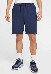Granatowe szorty dresowe z elastycznym pasem, regulowanym sznurkiem, bocznymi kieszeniami i czarnym logo Nike na lewym nogawce.