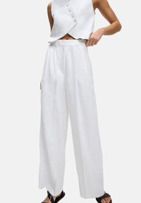 Witte linnen wijde broek met een hoge taille, voorzien van zijzakken en een gladde textuur, gecombineerd met een witte mouwloze top en zwarte sandalen.