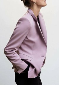 Blazer lilas sur mesure avec col châle, deux poches latérales et lignes élégantes et structurées. Le tissu a une texture lisse.