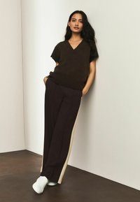 Brun kortærmet sweater med V-hals, kombineret med mørkelilla viddebukser med cremefarvet sideliste og hvide sneakers.