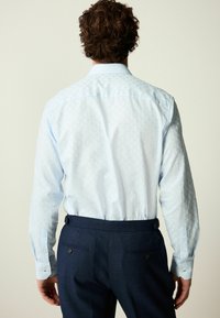 Lichtblauw overhemd met lange mouwen en een subtiel ruitpatroon, voorzien van een klassieke kraag en knoopmanchetten, gedragen met donkere broek.