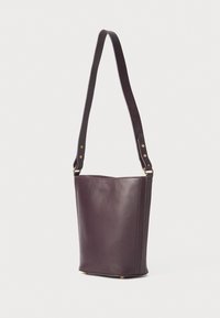 Bolso tipo cubo de piel morada con base plana, correa de hombro ajustable y acentos de hardware en tono dorado. Textura suave y diseño minimalista.
