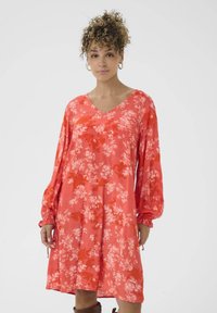 Blumenkleid in lebhaftem Korallenrot, mit V-Ausschnitt und langen Puffärmeln. Aus leichtem Stoff mit weicher Textur hergestellt.