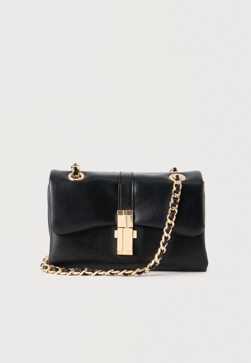 Melna ādas plecu soma ar zelta tonī ķēdes siksnu un taisnstūrveida zelta sprādzi, uz gaišas vienkrāsainas fona.