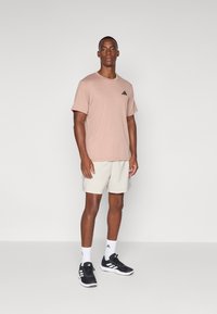 Ljust rosa sportt-shirt med en svart logo, tillsammans med beige shorts. Svarta sportskor och vita strumpor kompletterar outfiten.