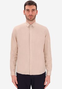 Camicia beige chiaro a maniche lunghe con bottoni, realizzata in tessuto testurizzato, dotata di colletto classico e chiusura frontale con bottoni.