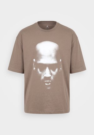 Ruskea lyhythihainen t-paita, jossa suuri vahvasti kontrastoitu valkoinen kasvokuva kaljulla päällä keskellä edessä.