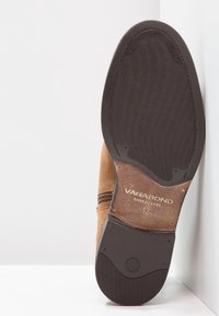 Bruna mockalädersankelboot med en texturerad svart gummisula, med subtila bruna accenter och varumärke på sulan.