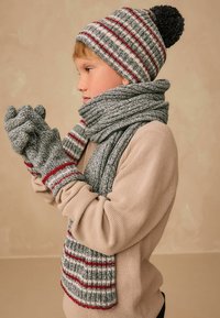 Grå og rød stribet strikhat med pompon, matchende tørklæde og handsker; tekstureret stof; hyggelige vintertilbehør til børn.