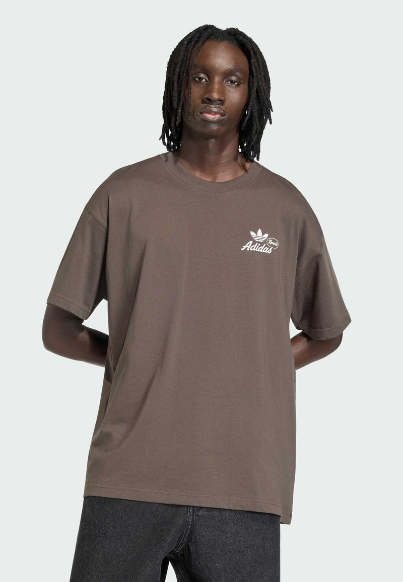 Maglietta di cotone marrone con maniche corte, scollo rotondo e logo Adidas bianco sul petto sinistro. Tessuto liscio, vestibilità rilassata.