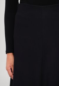 Musta hame, jolla on sileä pinta ja hienovarainen kuvio, puolipitkä, varustettuna tiukalla vyötäröosalla ja suoralla siluetilla.