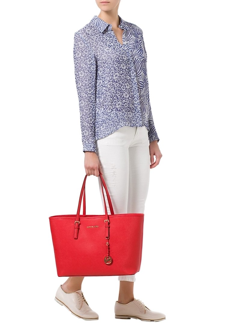 Rode neplederen tote bag met twee banden en een metalen logo, gecombineerd met een blauw patroon blouse en witte jeans.