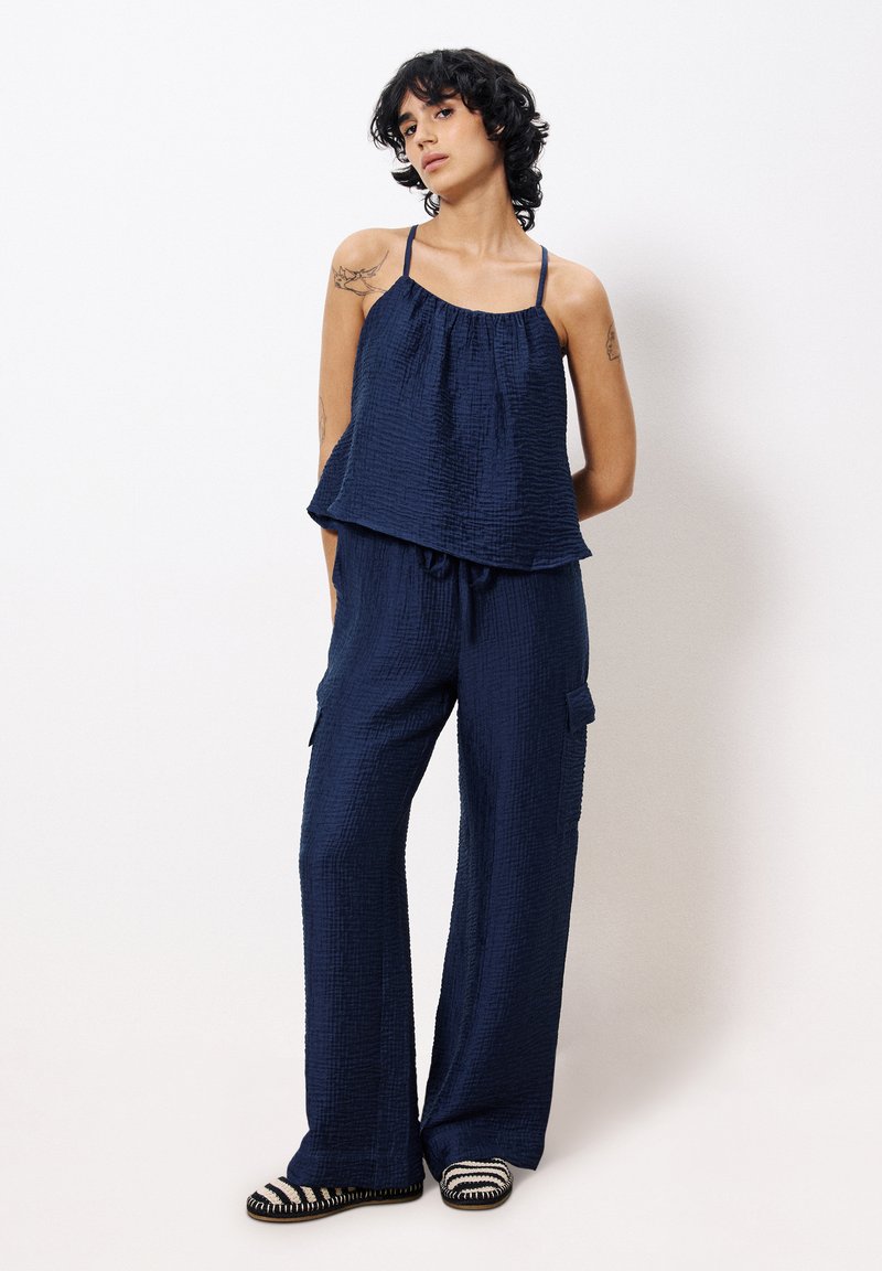Ensemble en deux pièces de couleur bleu marine texturé, comprenant un haut sans manches avec des bretelles réglables et un pantalon à jambes larges avec des poches latérales.