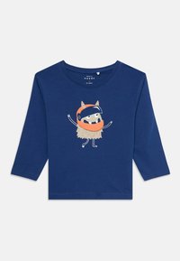 Sininen pitkähihaisen vauvan paita, jonka edessä on iloinen monsteri, jolla on oranssi kypärä ja harmaa karvainen vartalo.