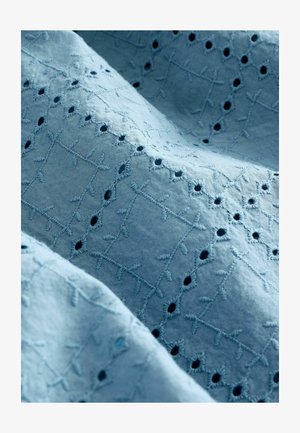 Tela azul clara con bordado intrincado, que presenta patrones de cruces y pequeños círculos recortados. Textura suave con un diseño delicado.