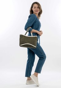 Borsa verde oliva con rifiniture in pelliccia sintetica bianca e doppi manici. Forma rettangolare, superficie liscia e bordi arrotondati.