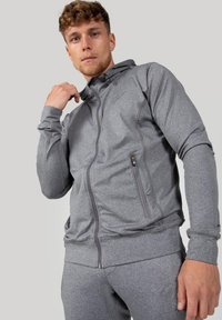 Grijze hoodie met rits, gemaakt van textuurstof, met een aansluitend ontwerp, zijzakken en een capuchon met trekkoord. Gebruiker draagt bijpassende broek.