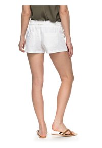 White linen shorts with an elastic waistband, two back pockets, and a loose fit, paired with brown flip-flops.