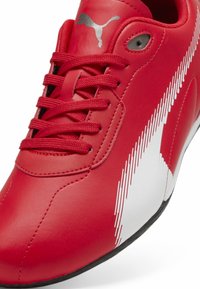 Sneaker rossa Puma con lacci rossi, logo Puma argentato sulla linguetta e design a striscia pixelata bianca lungo il lato e bordino nero.