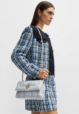 Hellblaue Lederhandtasche mit gestepptem Muster und goldenen Beschlägen, ausgestattet mit einer Kettenriemen für den Schultertrag, kombiniert mit einer blauen Tweedjacke.