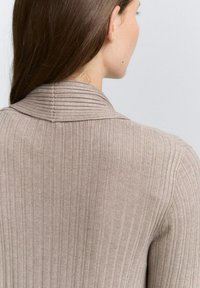 Beige gerippter Pullover mit umgeschlagenem Kragen und strukturierten Details auf der Rückseite, der eine taillierte Silhouette zeigt.