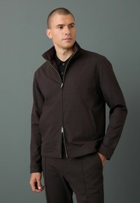 Brun zip-up jacka, mjukt tyg, hög krage, två framfickor, matchande byxor, glatt textur, enkel design, minimal hårdvara.