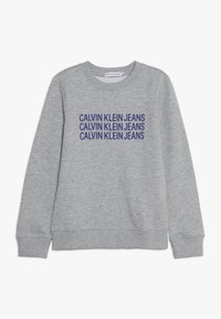 Szary sweter z miękkiego materiału z prążkowanymi mankietami i dołem. Na przodzie, wytłoczony na kolor niebieski, napis "CALVIN KLEIN JEANS".