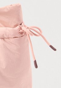 Vaaleanpunainen kangaskassi, jossa on kerätty yläosa, nyörikiristys ja ruskeat tipsit nyörissä pitämistä varten. Sileä rakenne.