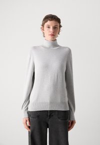 Jasnoszary sweter z golfem wykonany z miękkiego materiału, z długimi rękawami i ściągaczem, w komplecie z ciemnymi dżinsami.