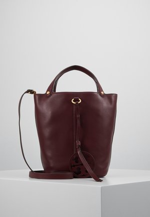 Sac à main en cuir bordeaux à texture lisse, avec un dessus arrondi et deux poignées. Comprend une bandoulière amovible et une étiquette décorative avec logo.