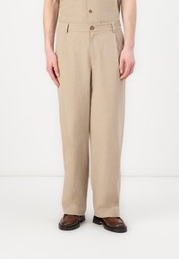 Pantaloni bej dintr-un material texturat, cu o croială lejeră, picioare drepte și închidere cu nasture la talie. Pantofii maro completează look-ul.
