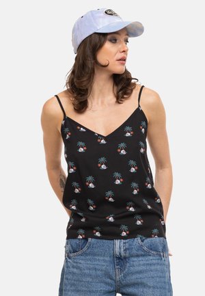 Femme portant un top noir à fines bretelles avec motif de palmier et de crâne, casquette bleue tie-dye et jean bleu, regardant sur le côté.