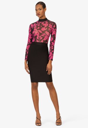 Maglietta a maniche lunghe in tessuto trasparente nero con un motivo floreale rosa, abbinata a una gonna a tubino nera aderente e sandali neri con cinturino.