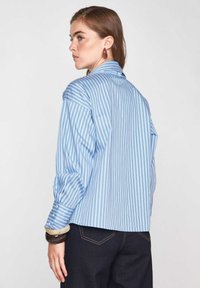 Camicia a righe blu e bianche con vestibilità rilassata, colletto con bottoni e maniche lunghe. Il tessuto è liscio con una trama leggera.