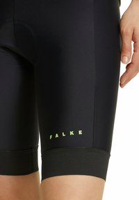 Pantaloni ciclistici neri con inserto imbottito, dotati di un logo verde "FALKE". Realizzati in tessuto liscio con una vestibilità aderente e orli elasticizzati.