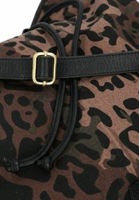 Mochila de lona con un patrón de estampado de leopardo en tonos marrón y negro, que cuenta con una correa de cuero negro y un cierre de hebilla dorada.