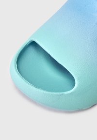 Slystanti į batą nuo aquos mėlynos iki šviesiai mėlynos spalvų gradiento, su tekstūruotu matinio paviršiaus apdaila. Atviras batų pirštas su apvalia forma ir minkštais kraštais.