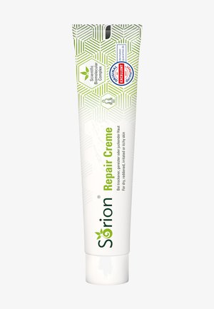 Die Sörion Repair Creme in einer weißen Tube zeigt grün-weiße geometrische Muster, hat einen Klappdeckel und Etiketten, die ihre Anwendung und Vorteile angeben.