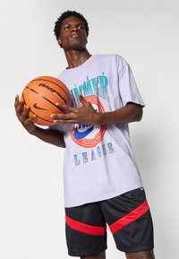 Lyse lilla grafisk t-shirt med teksten "SLAMMER LEAGUE", parret med sorte shorts med røde striber. Holder en orange basketball.