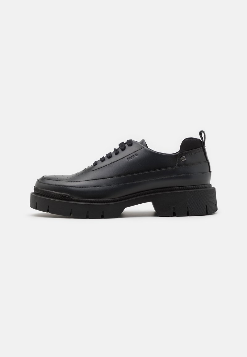 Chaussure en cuir noire à lacets avec semelle épaisse et languette à l'arrière, vue de profil sur fond blanc.