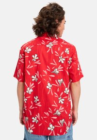 Camisa corta roja de manga corta con un patrón floral que presenta flores blancas y amarillas con acentos verdes, hecha de un tejido liviano.