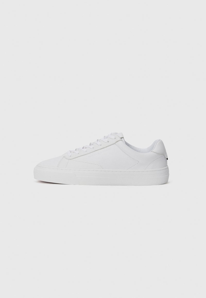 White low-top sneakers made of smooth leather, featuring a rounded toe, flat laces, and a textured rubber sole. Minimalist design with no visible branding.