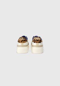 Baskets à plateforme blanches avec détail imprimé léopard et logo « Buffalo » sur le talon, vues de dos sur un fond gris uni.