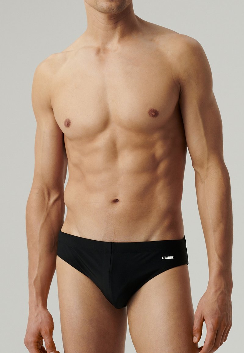 Czarne slipki kąpielowe wykonane z gładkiego materiału, charakteryzujące się niskim stanem i subtelnym logo z przodu. Klasyczny design kostiumu kąpielowego.