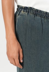 Denim bukser med en samlet talje, i en mørkeblå farve og synlige sømdetaljer. Glat tekstur med en afslappet pasform.