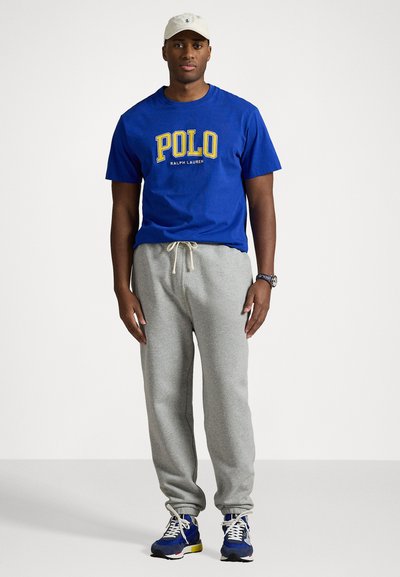 Royal blue cotton t-shirt with yellow "POLO RALPH LAUREN" logo, paired with light gray sweatpants and blue athletic sneakers.