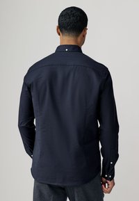 Camicia blu navy con bottoni, maniche lunghe, tessuto liscio, leggero lucido, polsini con doppio bottone e colletto classico.